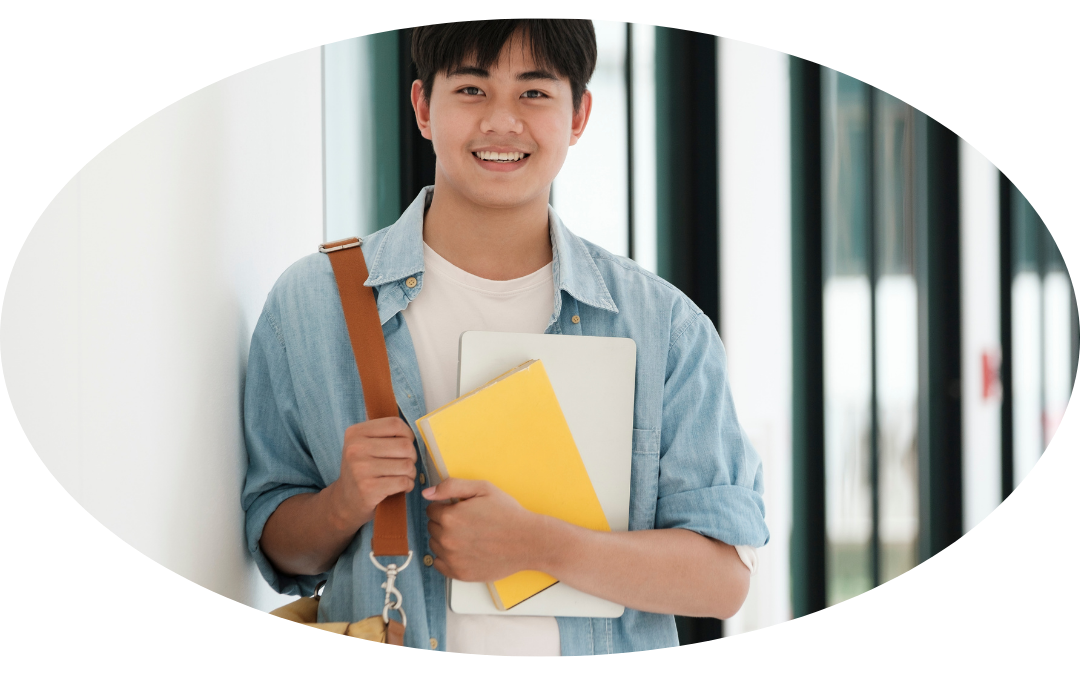 This is an oval image of a man smiling, standing in a hallway holding a satchel and two notebooks.
